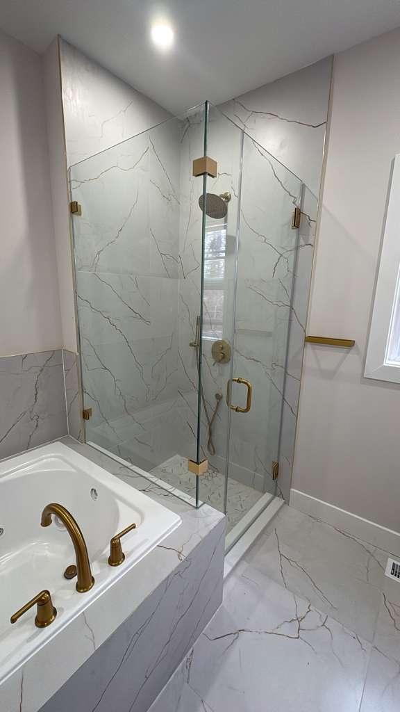 Corner frameless shower with brushed gold hardware beside a tub