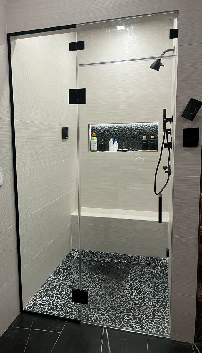 Frameless shower door with matte black hinges and black pebble floor