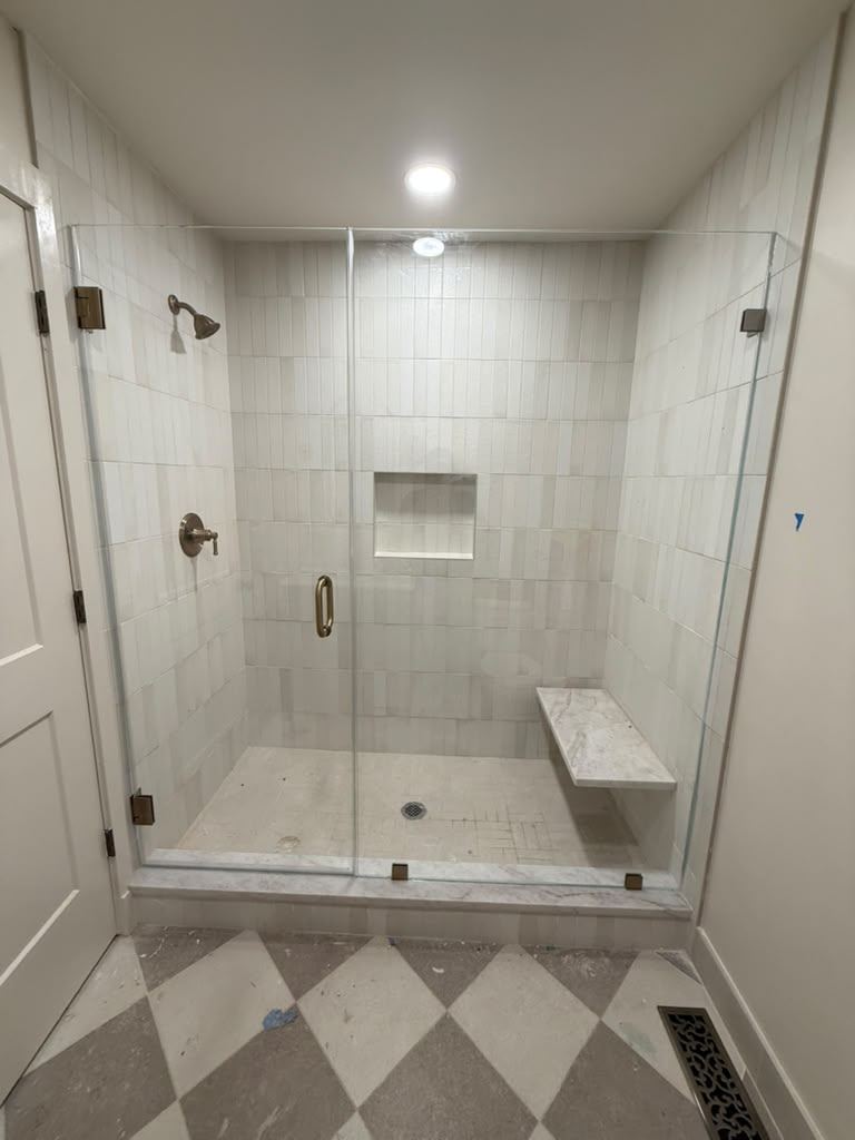 Frameless shower with brushed brass hardware and a floating bench