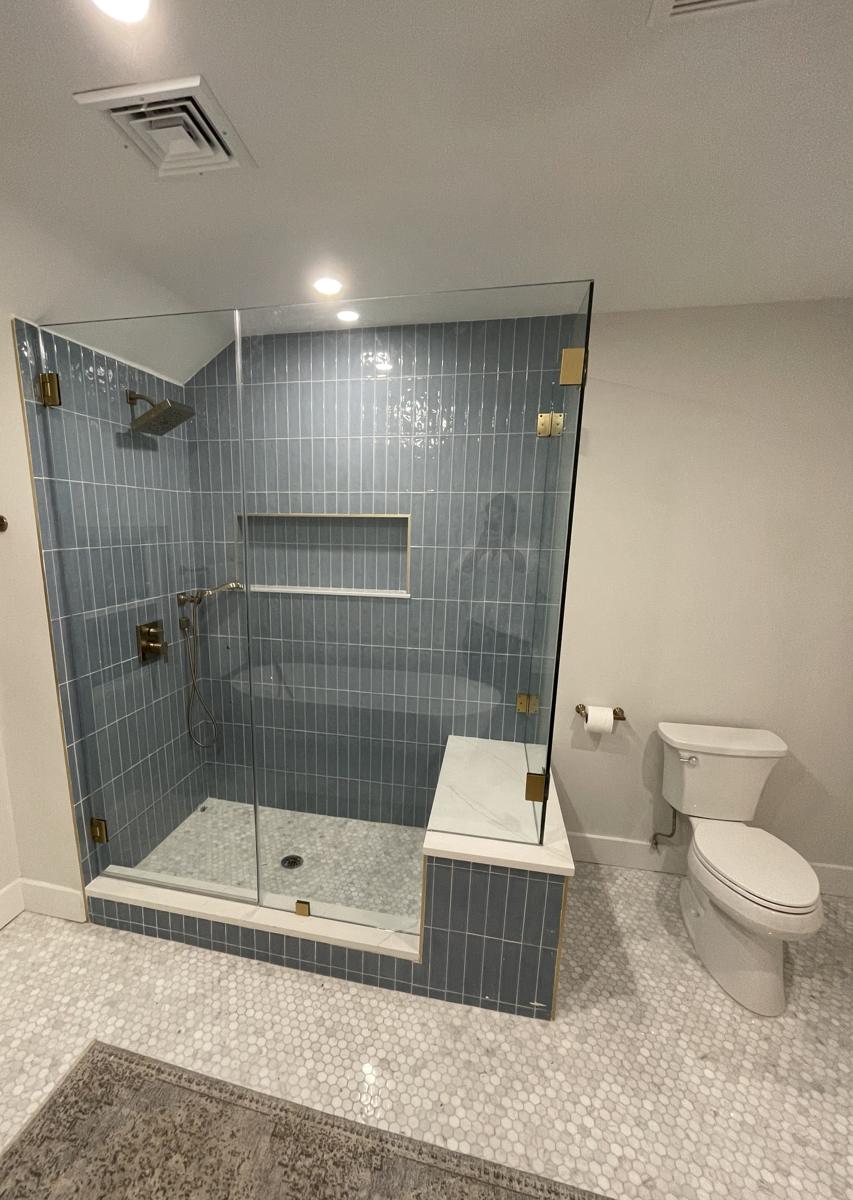 Frameless shower with brushed brass hinges and blue tile