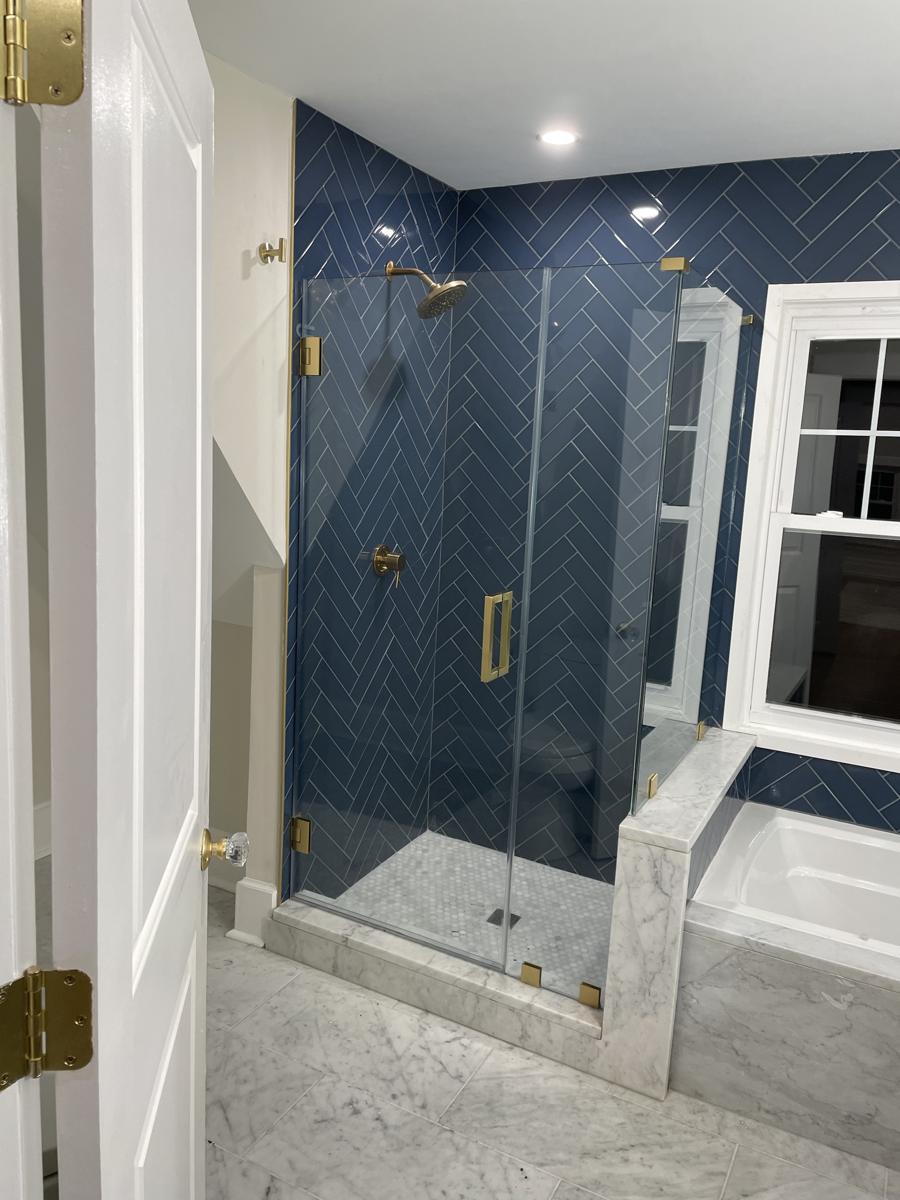 Frameless shower with brushed gold hardware and navy herringbone tile