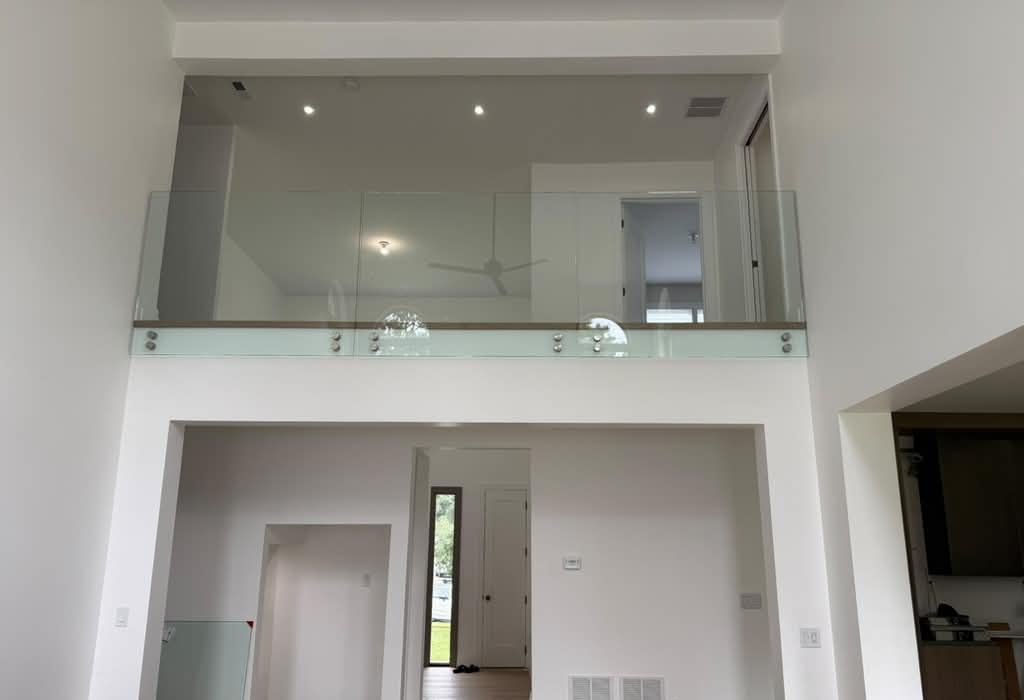Frameless glass loft railing on standoffs over a two-story living room