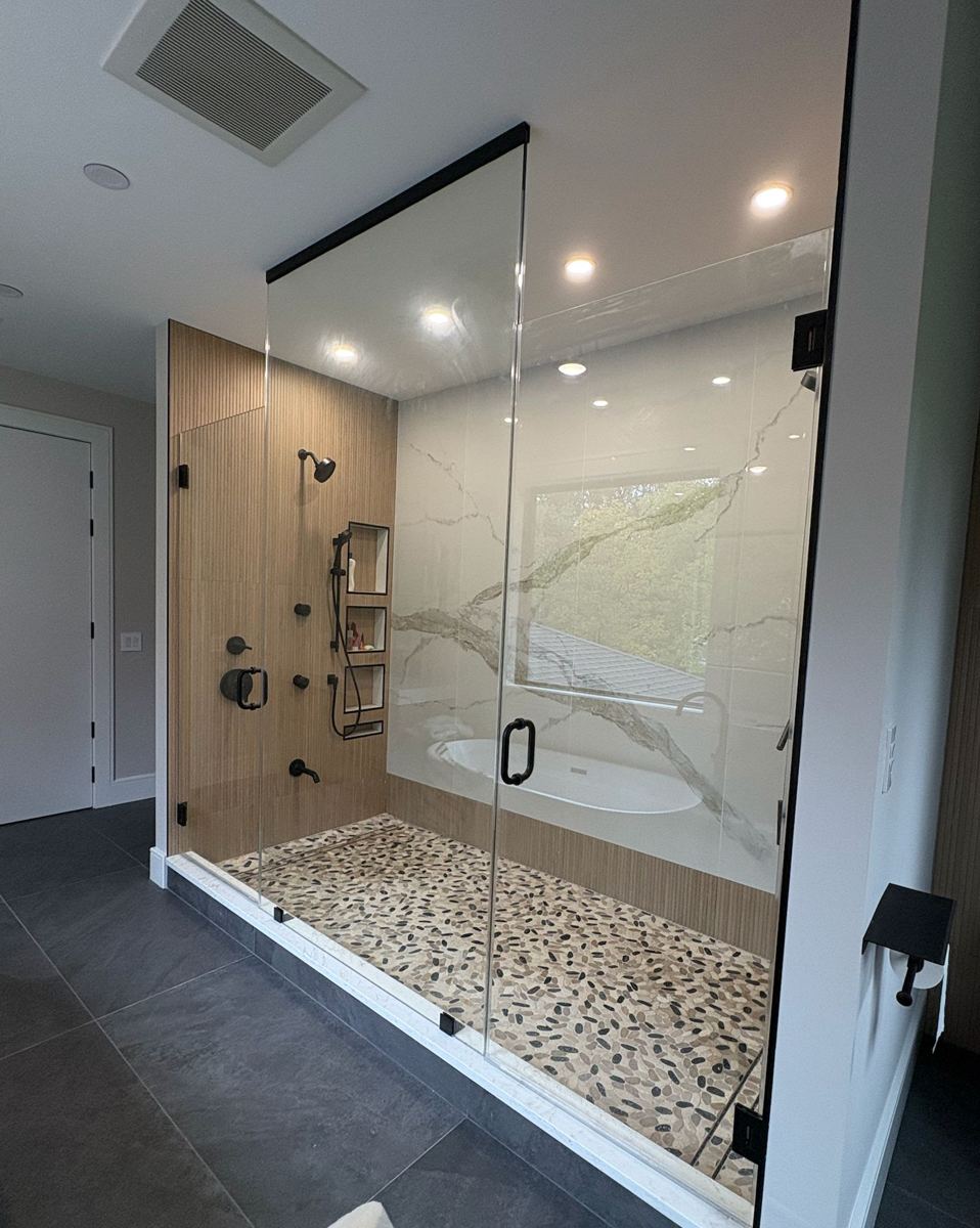 Large frameless shower with matte black header over a freestanding tub view