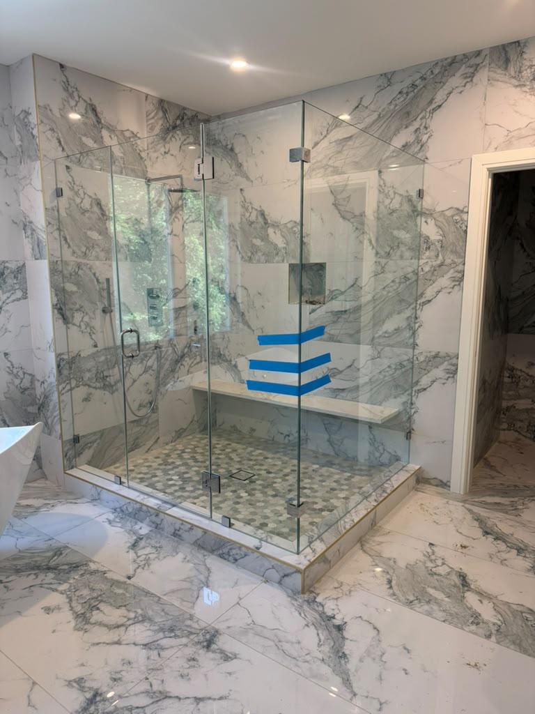 Large frameless shower enclosure with bench in a marble bathroom