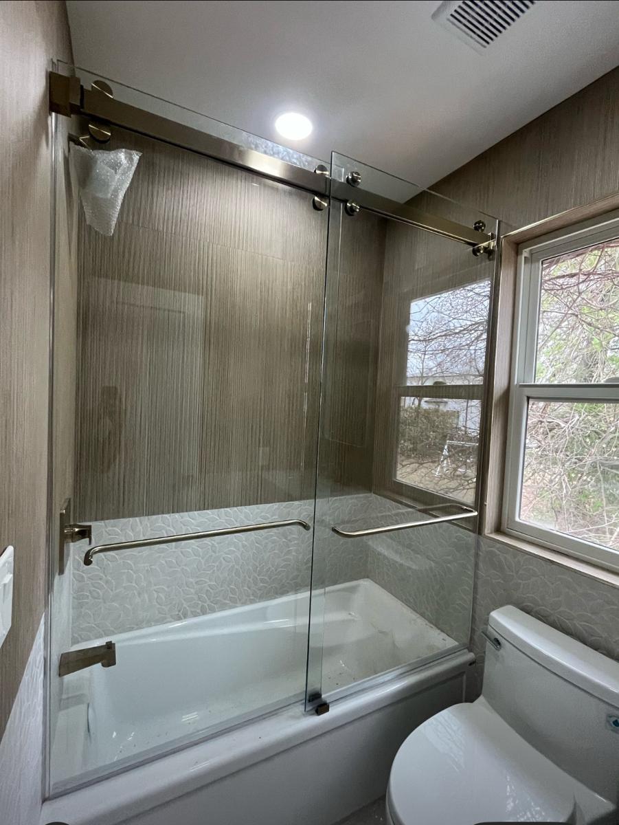 Frameless sliding tub door with brushed nickel hardware